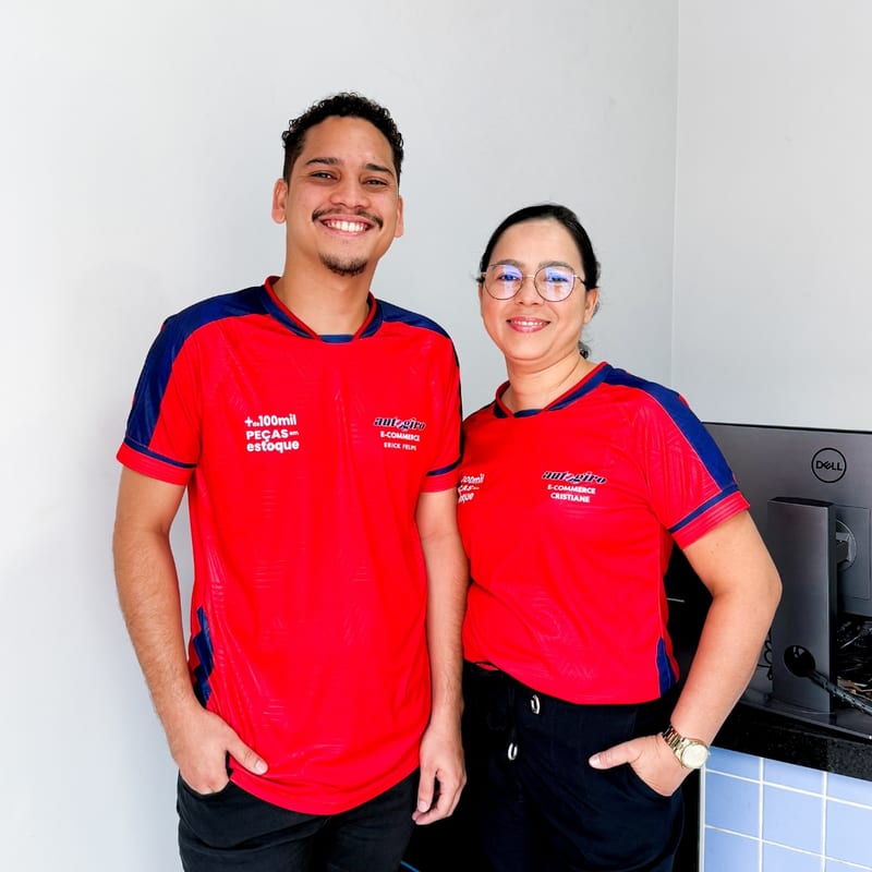Dois integrantes da equipe da Autogiro Ecommerce sorrindo, com o uniforme vermelho e azul da marca