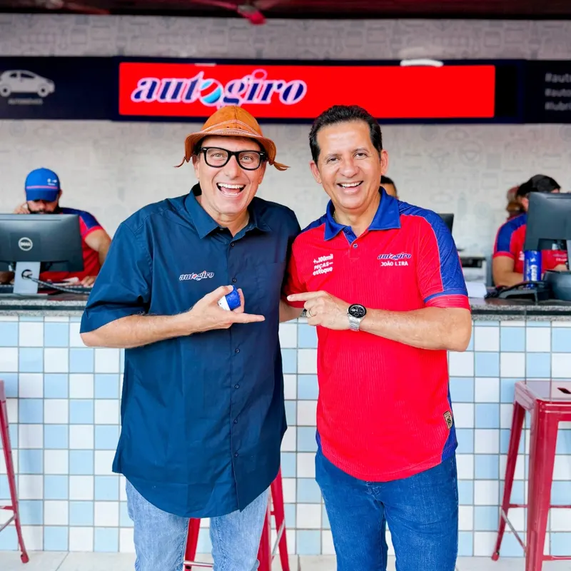 Dois integrantes da Autogiro sorrindo em frente ao letreiro luminoso da loja